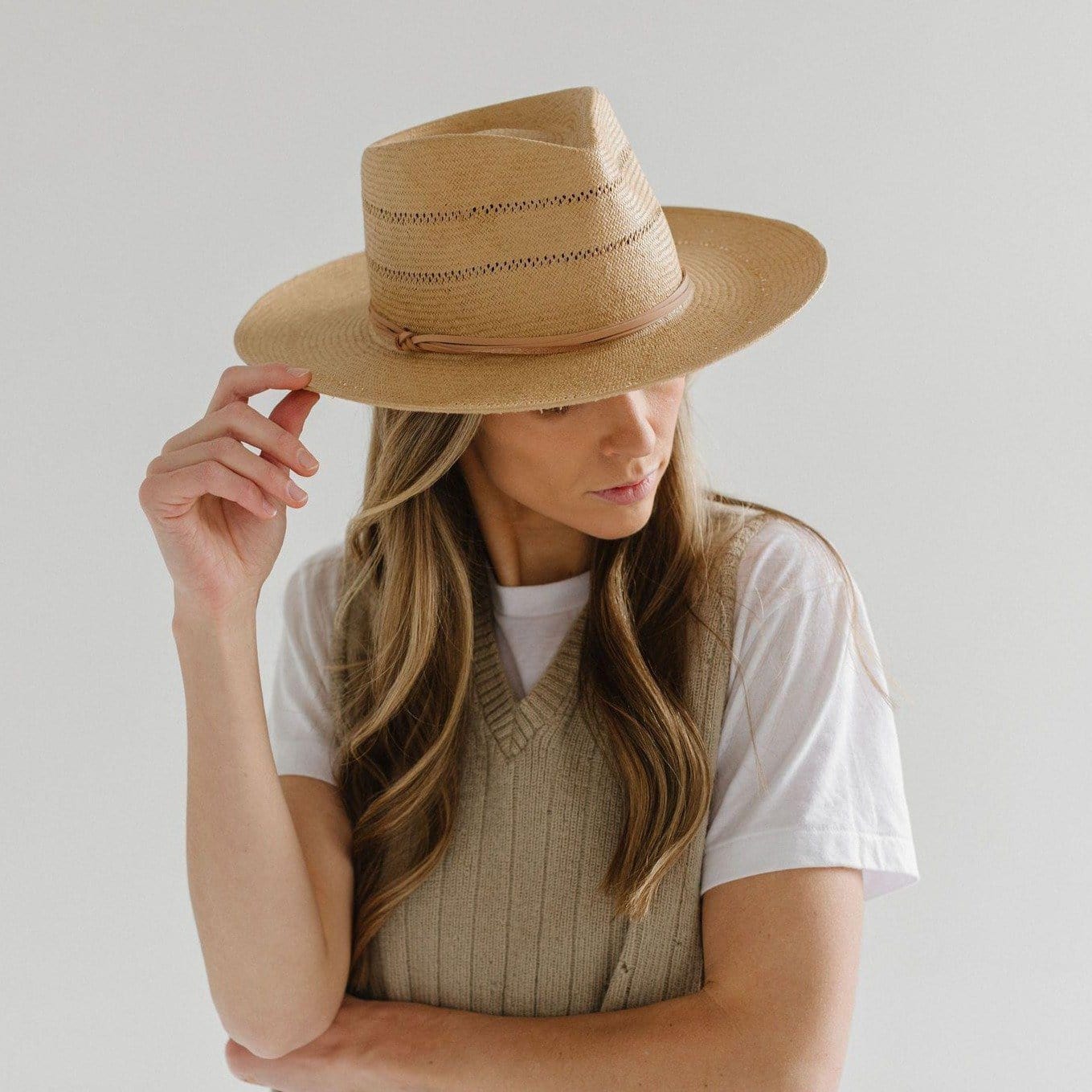 Woman wearing a honey colored fedora straw hat with a hat band and a beige sweater against a plain background #color_honey
