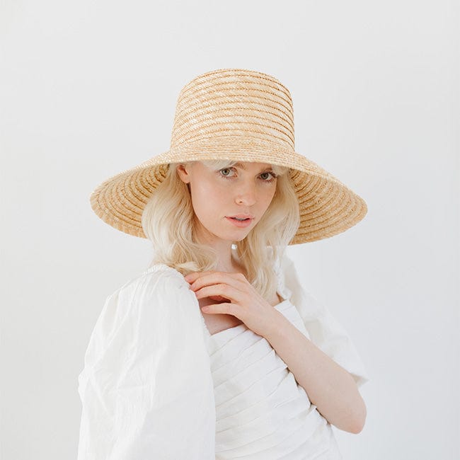 Woman wearing a natural colored straw boater hat and a white top against a plain background  #color_natural