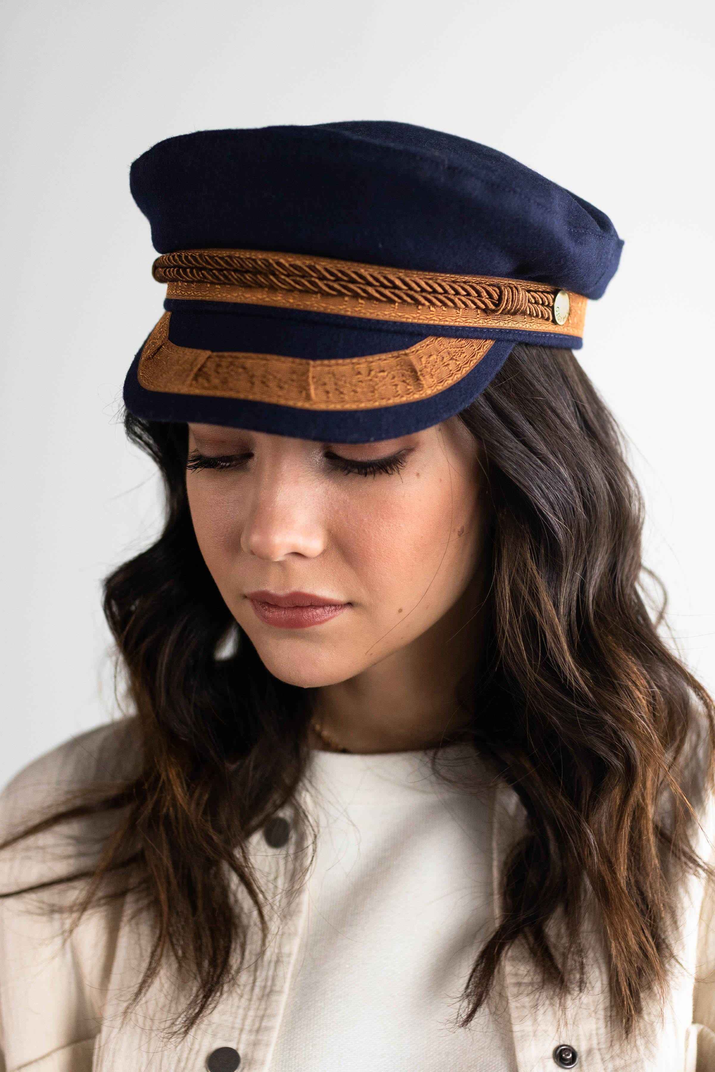 Close up image of a woman wearing a navy and gold colored lieutenant cap and a white t-shirt inside a cream shirt against a plain background #color_navy