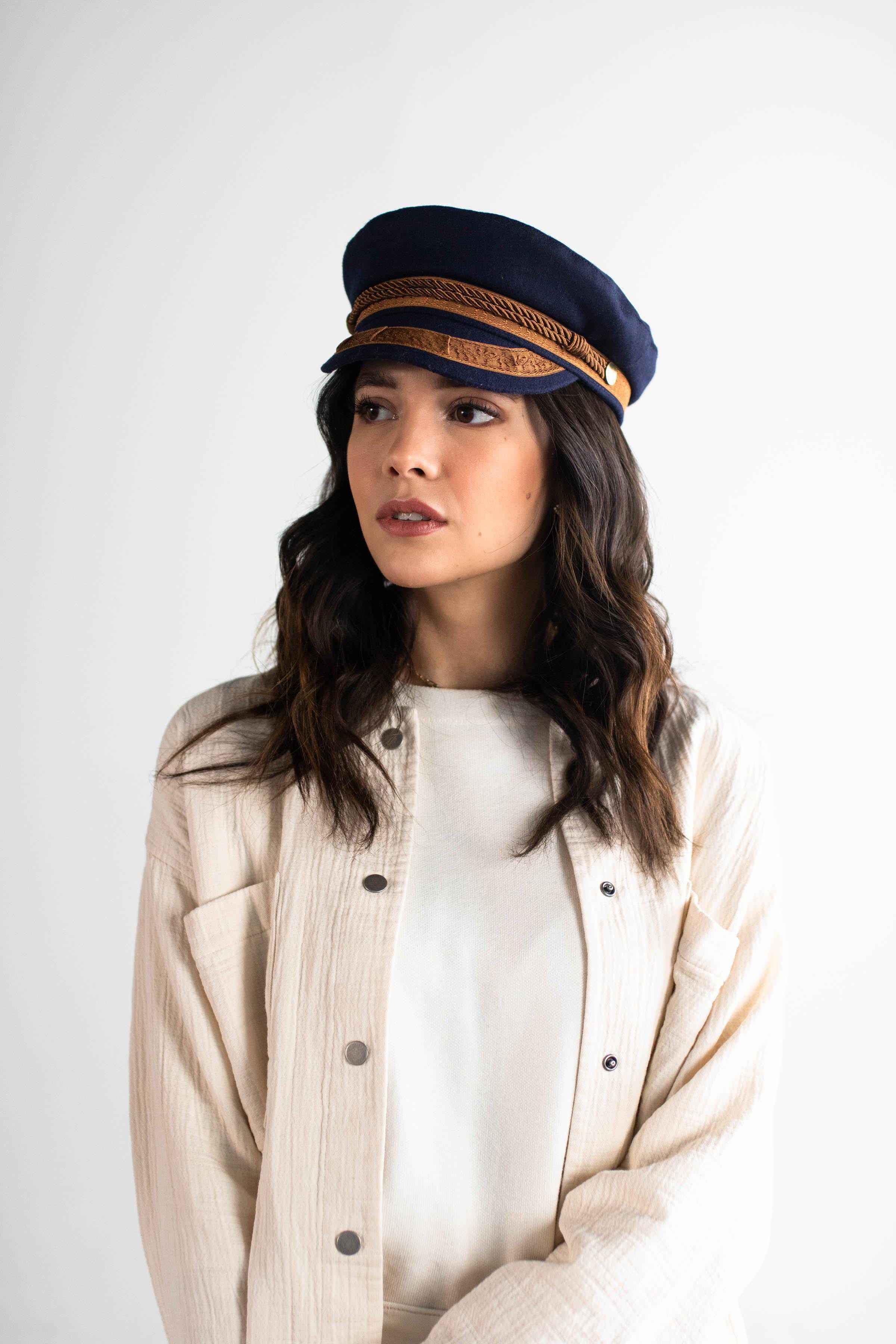 Woman wearing a navy and gold colored lieutenant cap and a white t-shirt inside a cream shirt against a plain background #color_navy