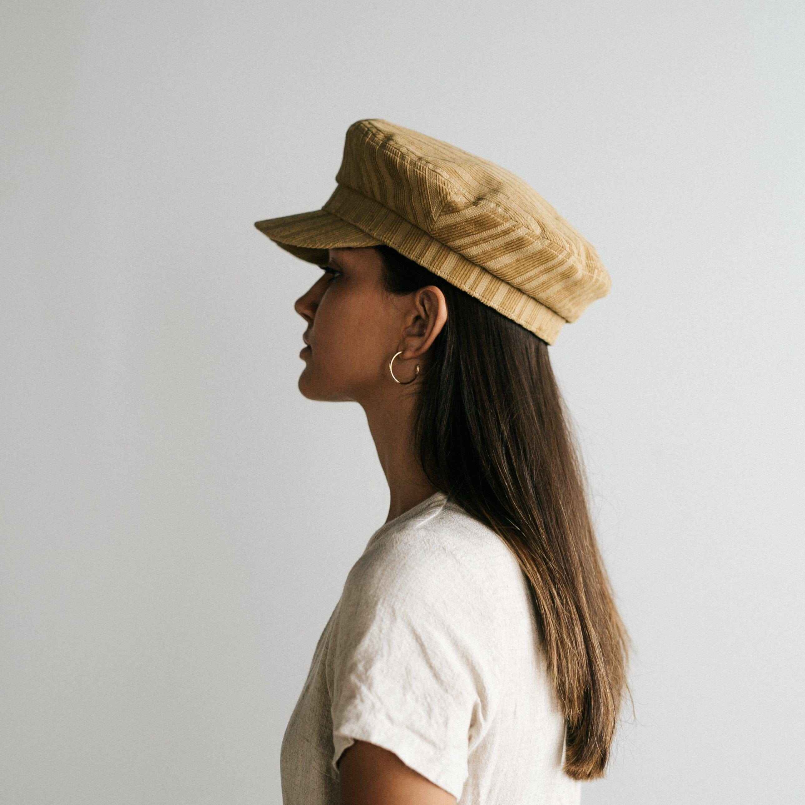 Woman wearing a mustard colored striped cap and a white t-shirt, facing sideways against a plain background  #color_mustard